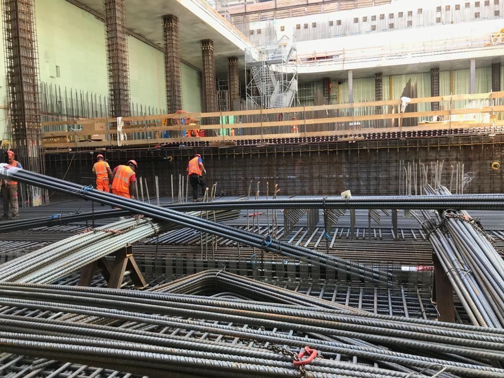 Eisenleger tragen lange Bewehrungsstäbe über die Baustelle